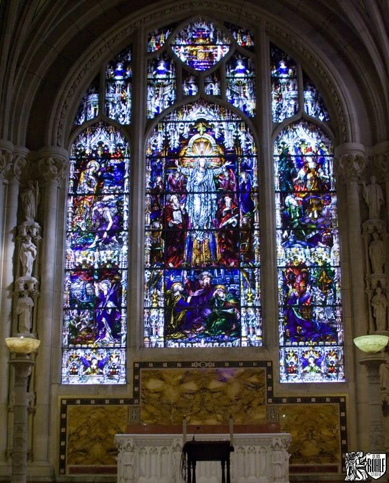The interior of the Cathedral of St John the Divine, New York, with a great stained glass window above the altar.
